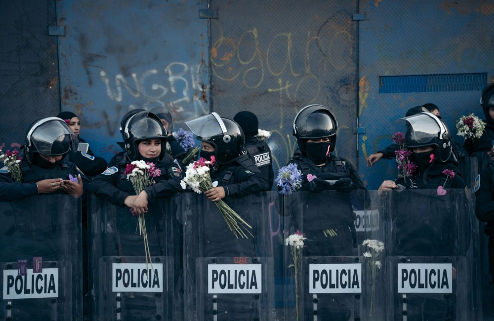 Police officers with flowers interact during Women's Day protest in Mexico City, highlighting solidarity.